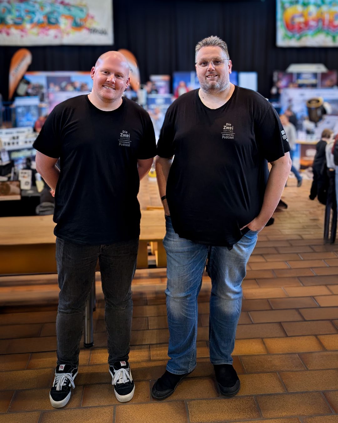 Tobi (links) und Sven (rechts) in schwarzen „Die Zwei vom Feld“-Shirts auf einer Astronomie-Messe